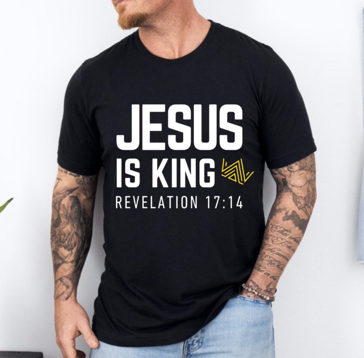 Black crewneck t-shirt that says, “Jesus is king” in large bold letters. There is a yellow geometrical crown. Underneath in smaller letters it says, “Revelation 17 14”.