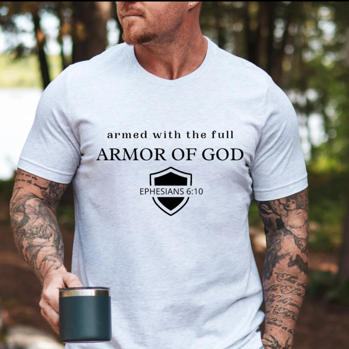 Ash white crewneck t-shirt that says, “armed with the full armor of God.” There is a shield with “Ephesians 6 10” running through the middle.