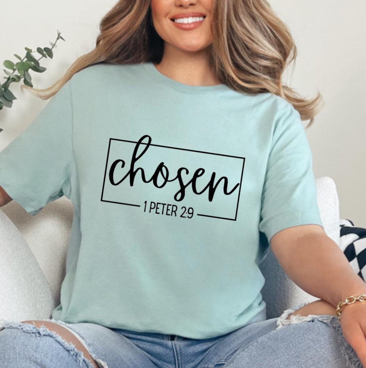 Dusty green crewneck t-shirt that says, “chosen” in large cursive letters. Underneath in smaller letters it says, “1 Peter 2 9.”