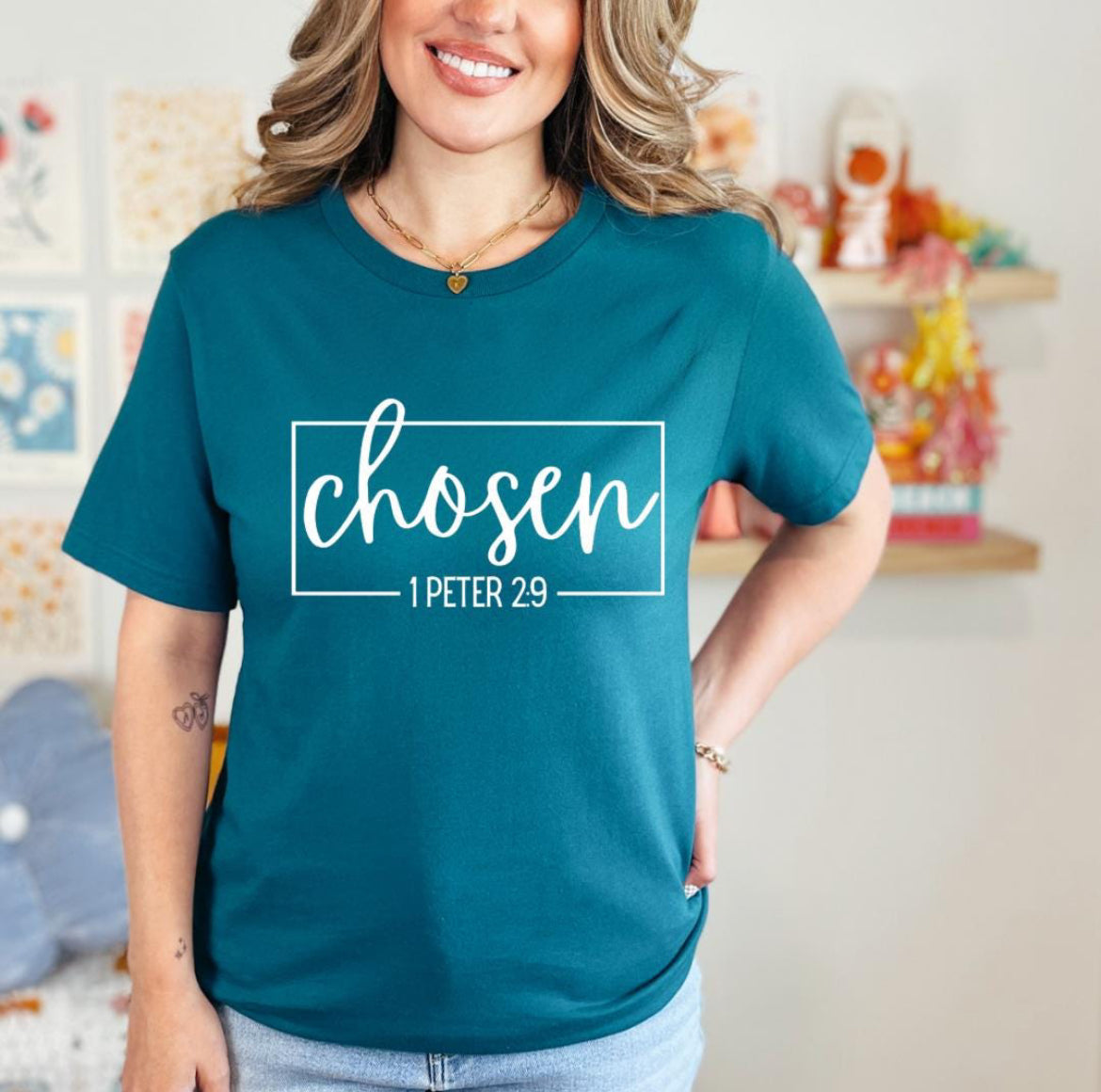 Deep teal crewneck t-shirt that says, “chosen” in large cursive letters. Underneath in smaller letters it says, “1 Peter 2 9.”