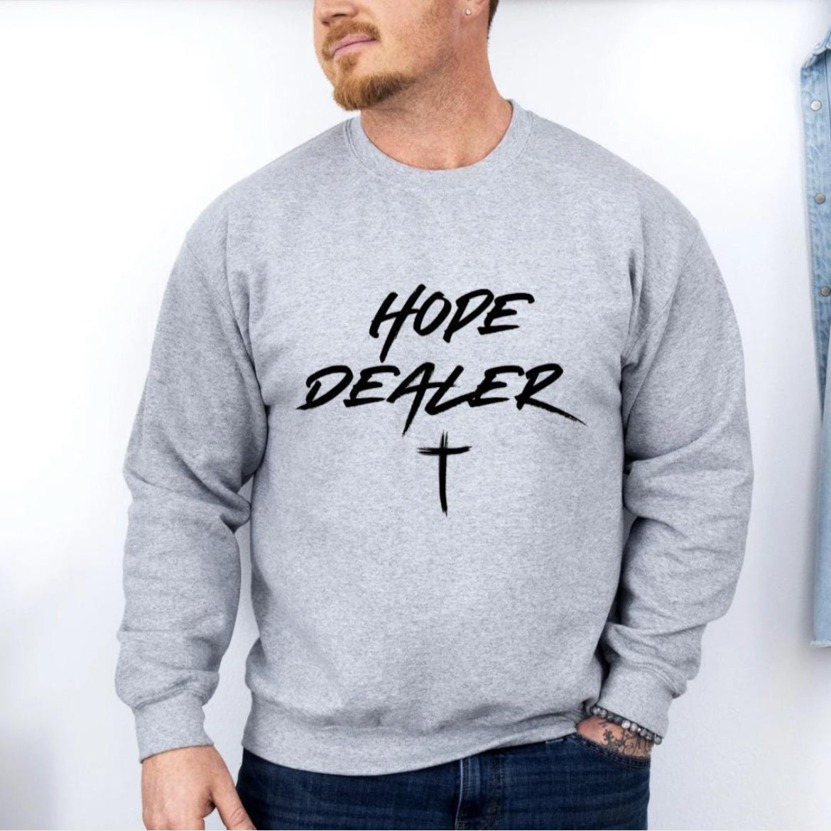 Grey crewneck sweatshirt that says, “Hope dealer” in graffiti style writing with a cross.