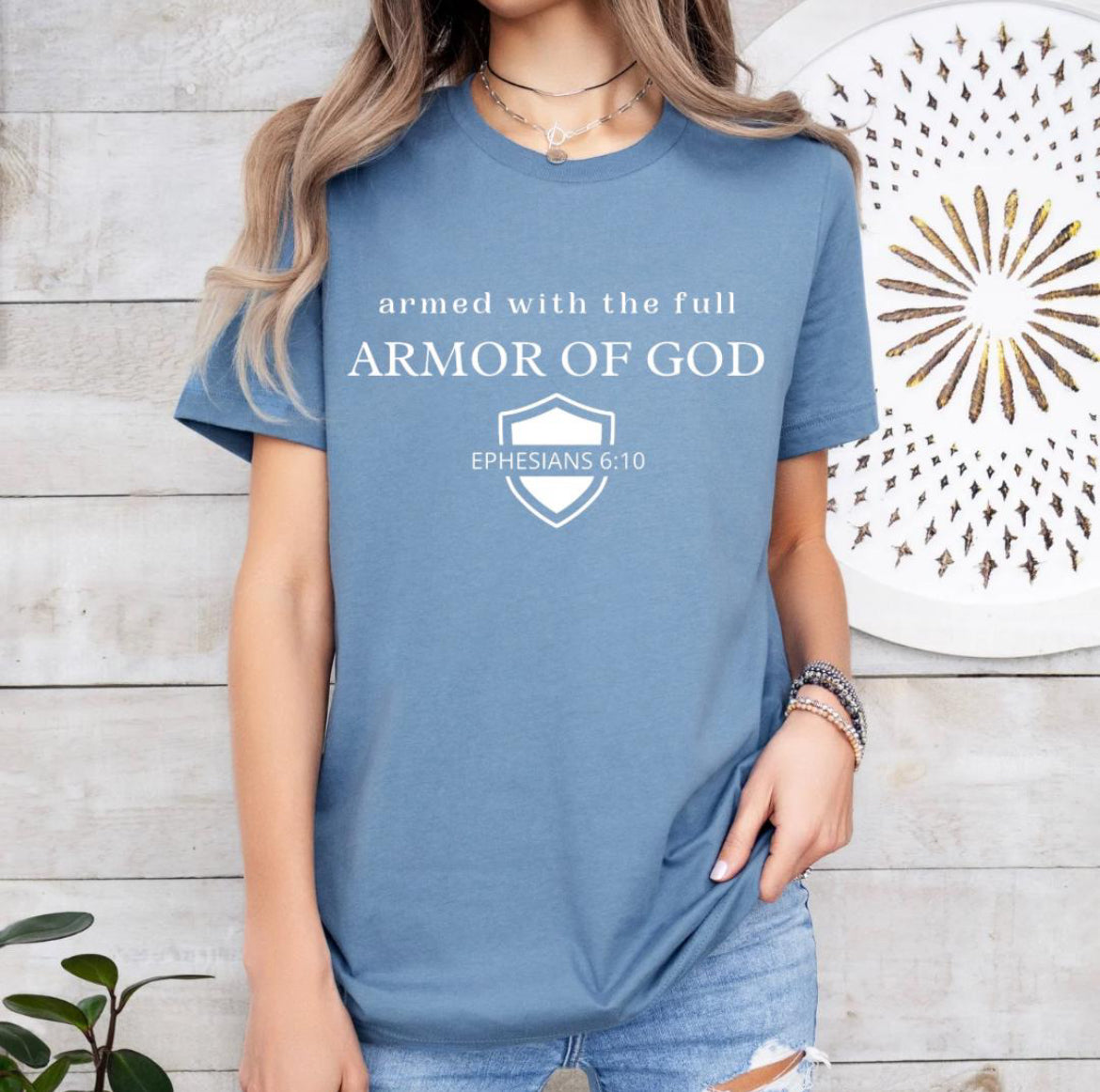 Steel blue crewneck t-shirt that says, “armed with the full armor of God.” There is a shield with “Ephesians 6 10” running through the middle.