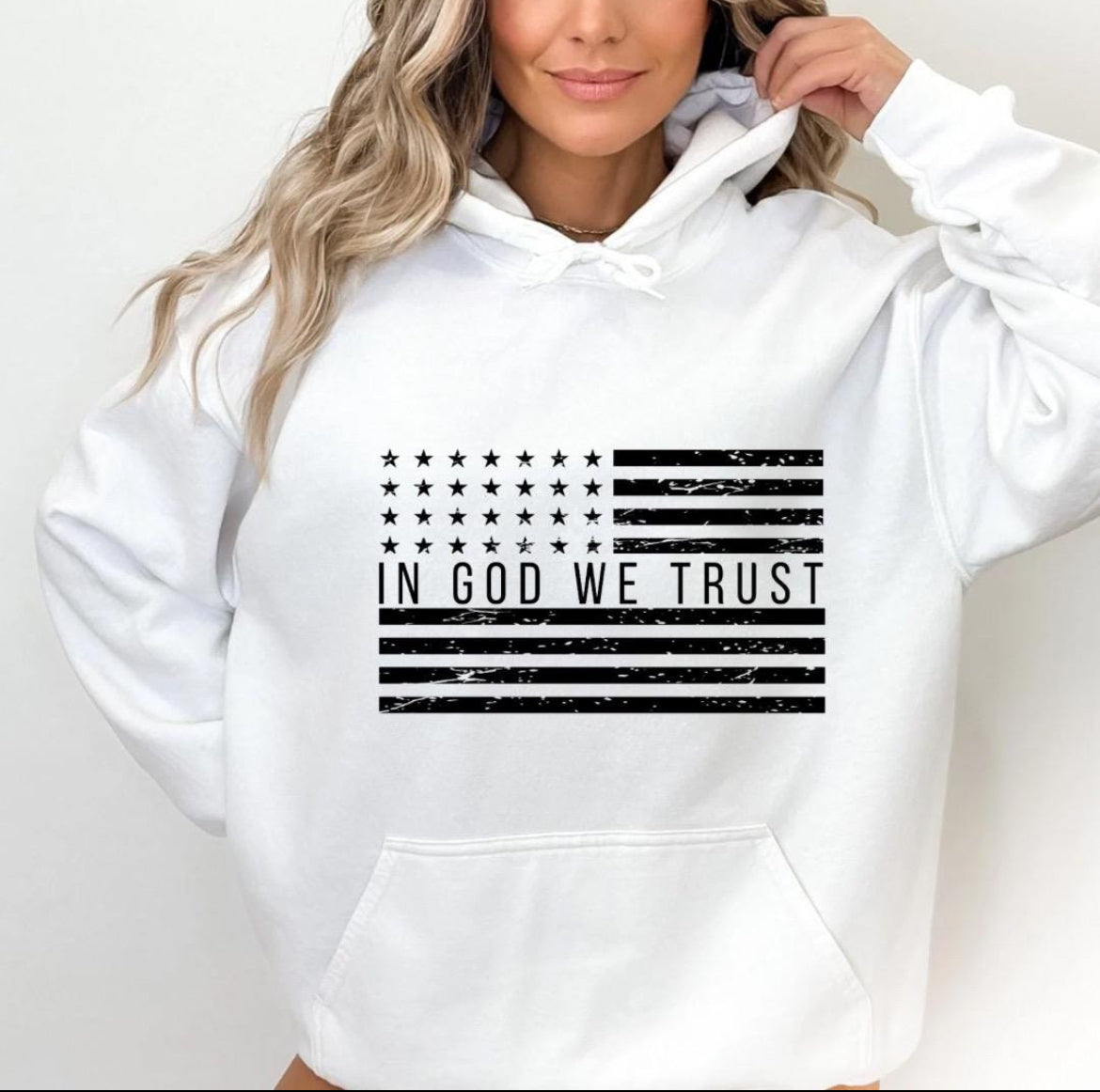 White hoodie with a distressed American flag that says, "In God we trust" across the middle of the flag.