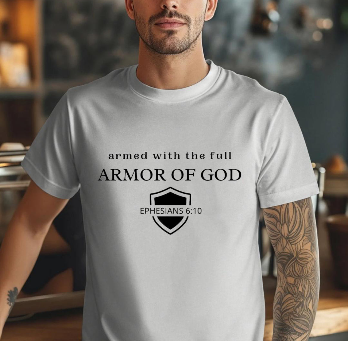 Gray crewneck t-shirt that says, “armed with the full armor of God.” There is a shield with “Ephesians 6 10” running through the middle.