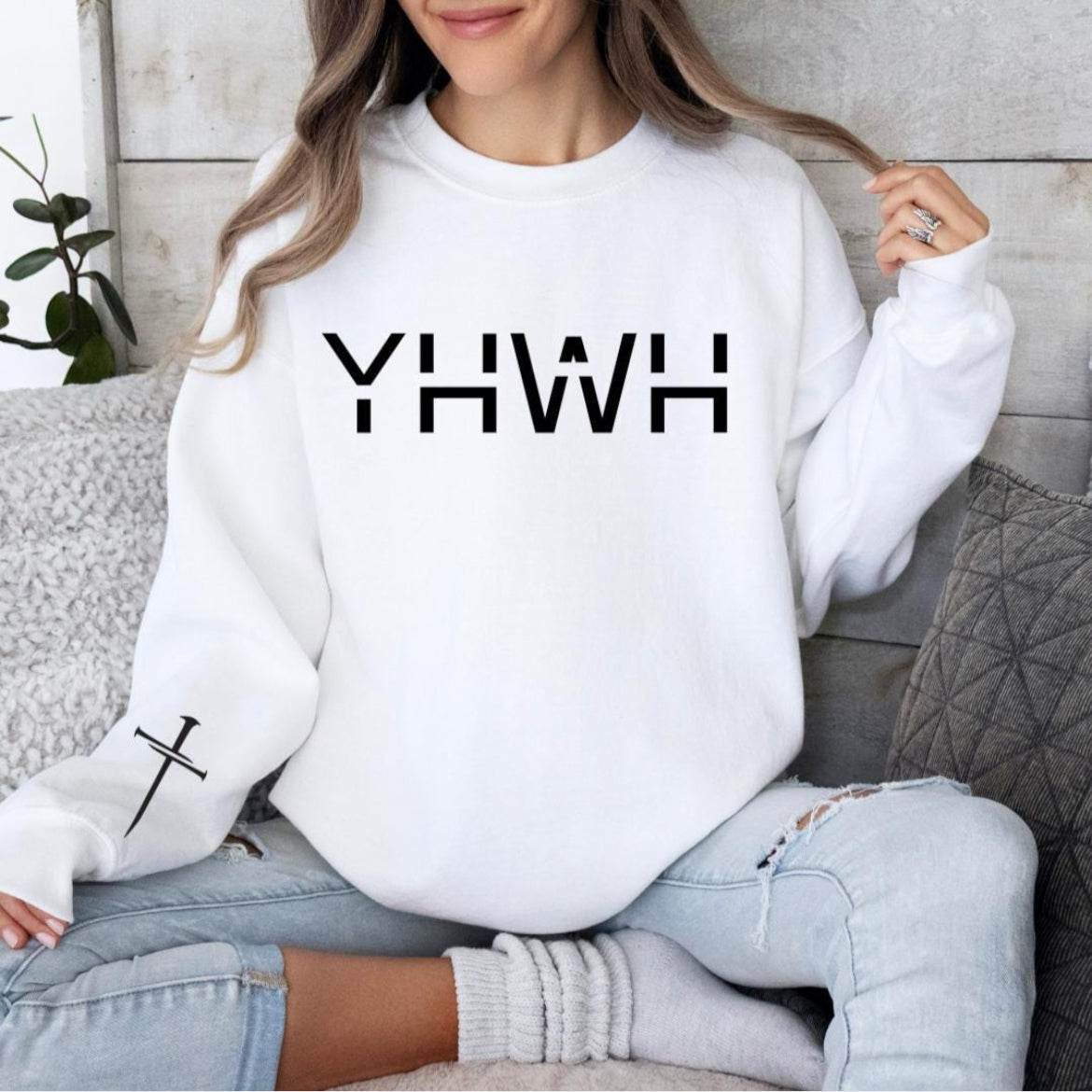 White crewneck sweatshirt that says, "YHWH" with a cross on the sleeve.