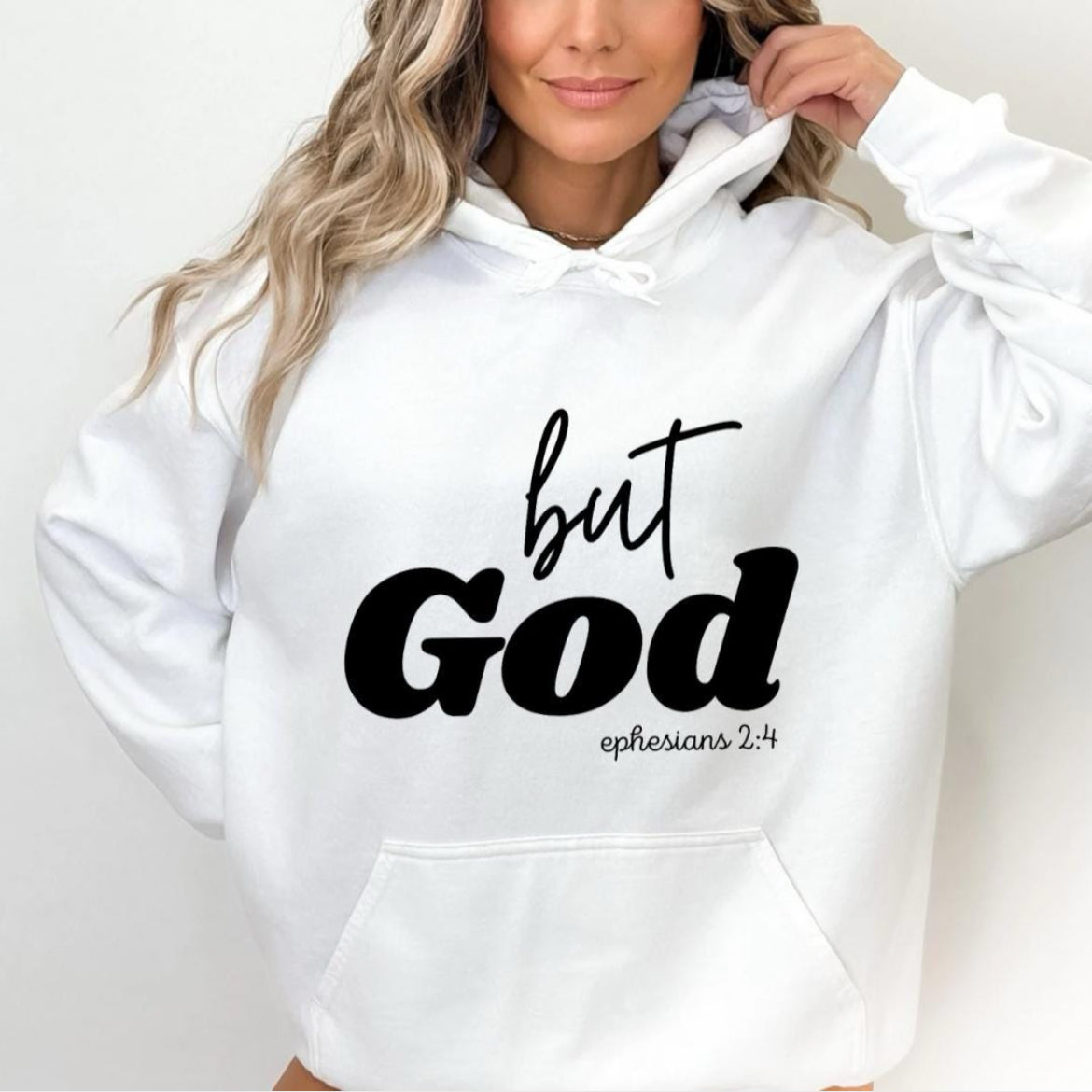 White hooded sweatshirt that says, "But God" in large letters. Underneath it says, "Ephesians 2 verse 4" in smaller letters.
