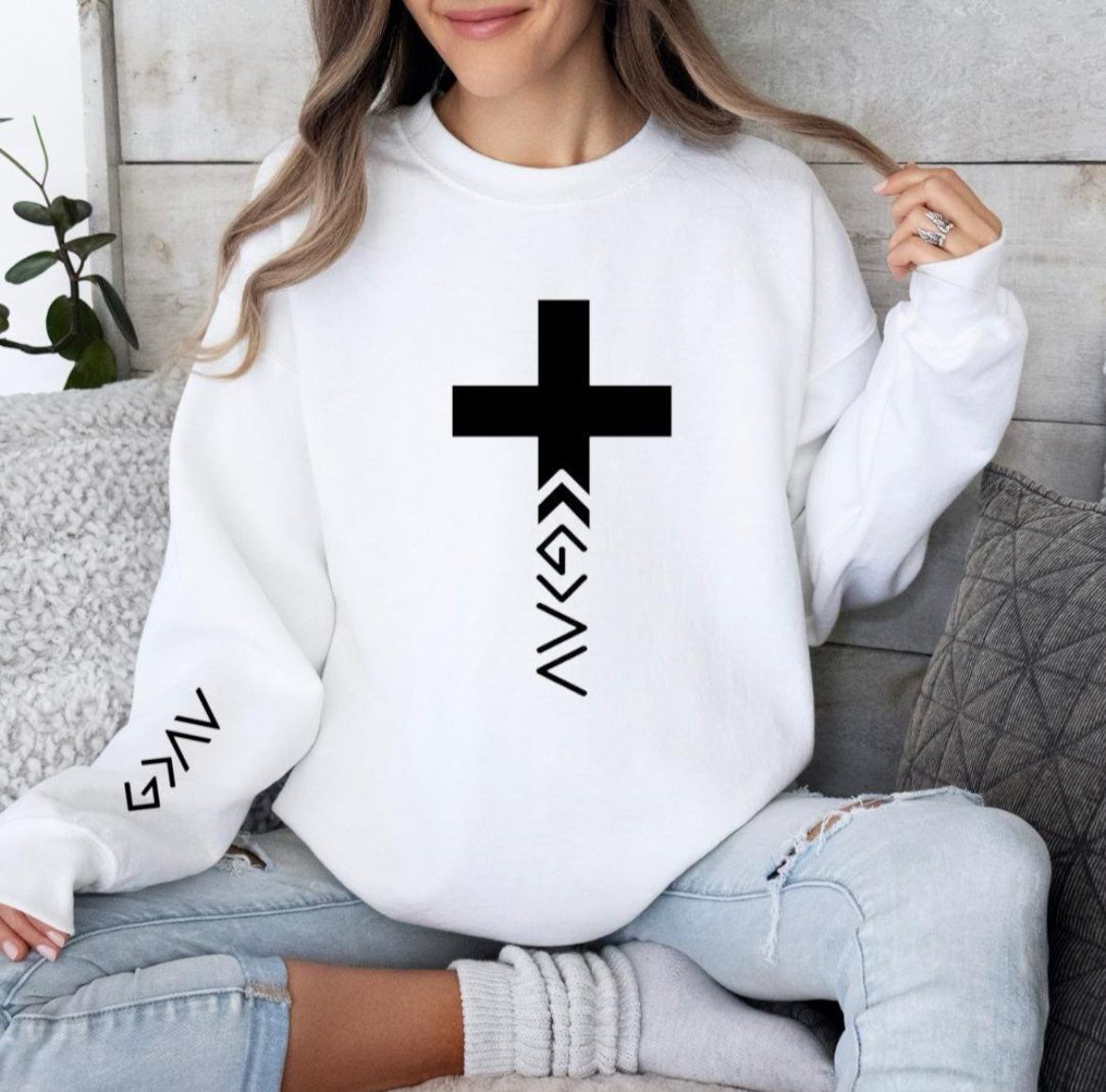 White crewneck sweatshirt that has a cross with the "God is greater than the highs and lows" symbol on the bottom. The same symbol is on the sleeve.