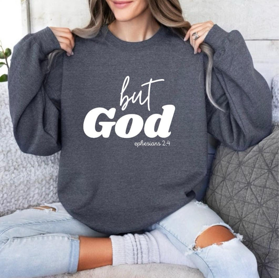 Dark gray heather crewneck sweatshirt that says, "But God" in large letters. Underneath it says, "Ephesians 2 verse 4" in smaller letters.