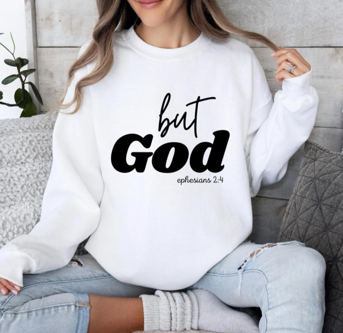 White crewneck sweatshirt that says, "But God" in large letters. Underneath it says, "Ephesians 2 verse 4" in smaller letters.