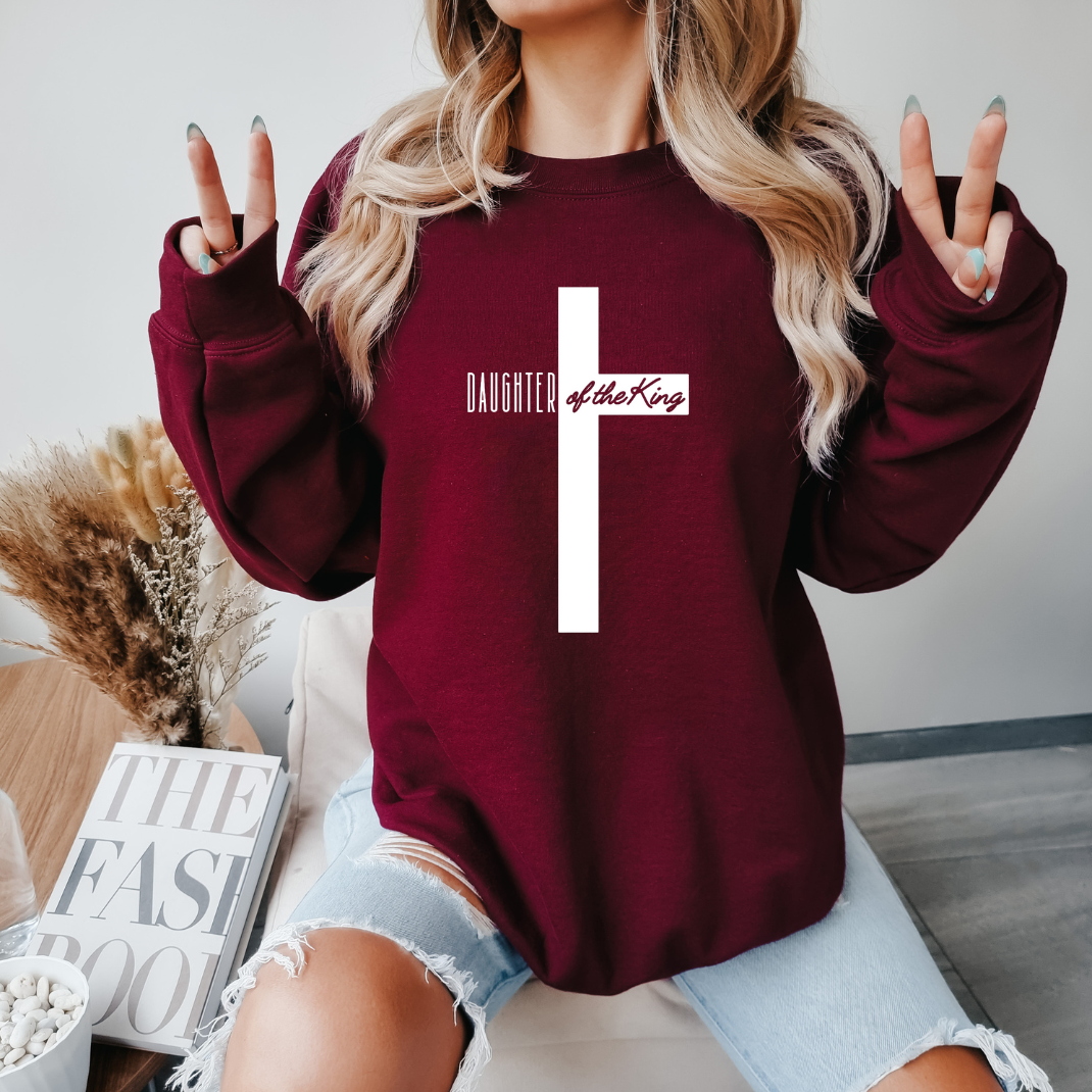 maroon crewneck sweatshirt that says, "daughter of the King" across the middle of a large cross.