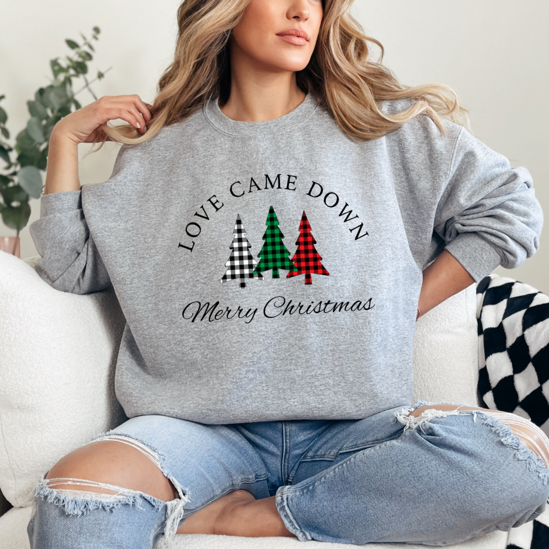 Grey crewneck sweatshirt that says, "Love came down. Merry Christmas" with three Christmas trees in buffalo plaid green, red and black.