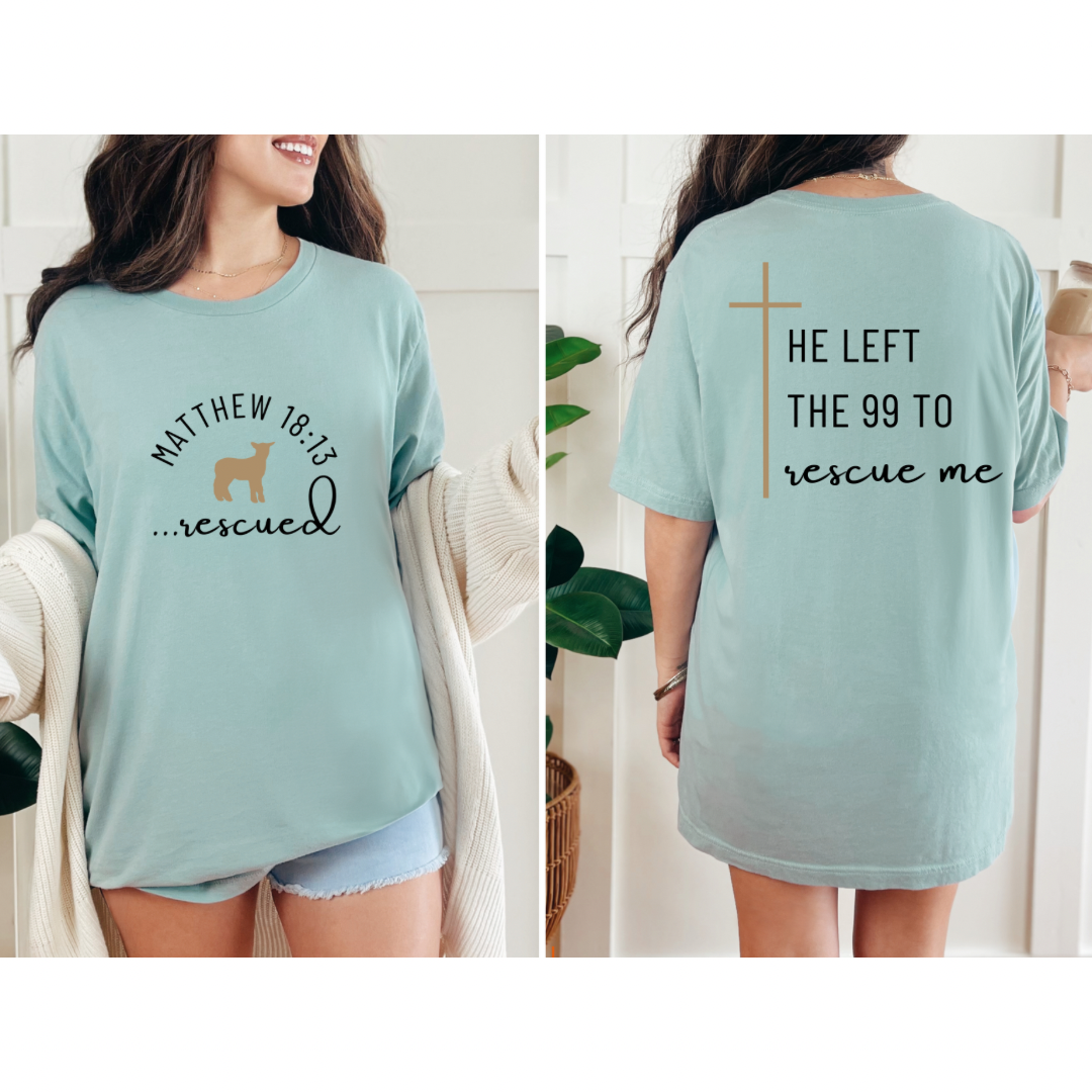 Dusty green crewneck T-Shirt that says, "He left the 99 to rescue me" with a large tan cross. On the front it says, "Matthew 18:13 rescued" with a tan sheep.