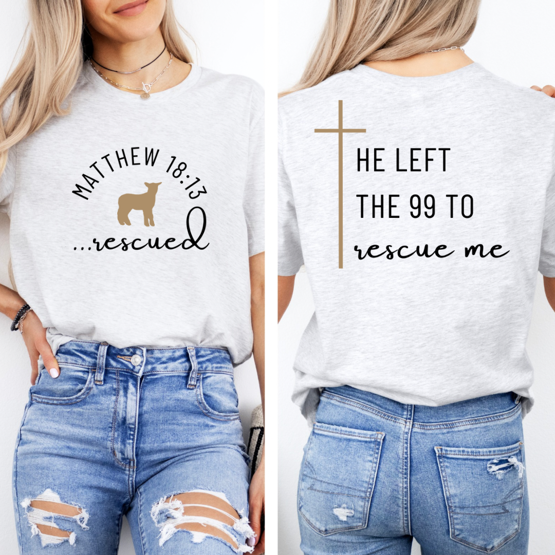 Ash white crewneck T-Shirt that says, "He left the 99 to rescue me" with a large tan cross. On the front it says, "Matthew 18:13 rescued" with a tan sheep.