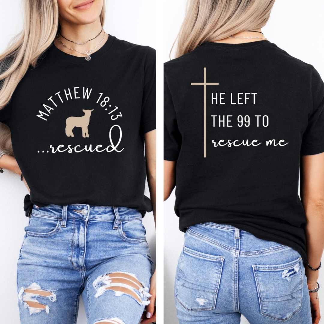Black crewneck T-Shirt that says, "He left the 99 to rescue me" with a large tan cross. On the front it says, "Matthew 18:13 rescued" with a tan sheep.