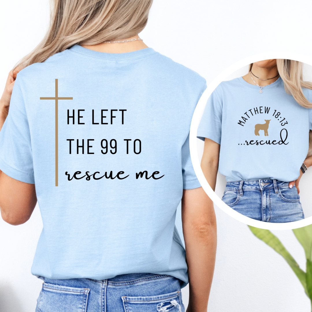 Baby blue crewneck T-Shirt that says, "He left the 99 to rescue me" with a large tan cross. On the front it says, "Matthew 18:13 rescued" with a tan sheep.