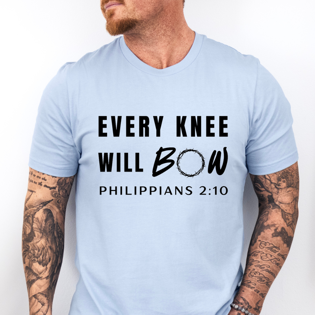 Baby blue crewneck t-shirt that says, “every knee will bow. Philippians 2:10” with a crown of thorns as the “o” in bow.