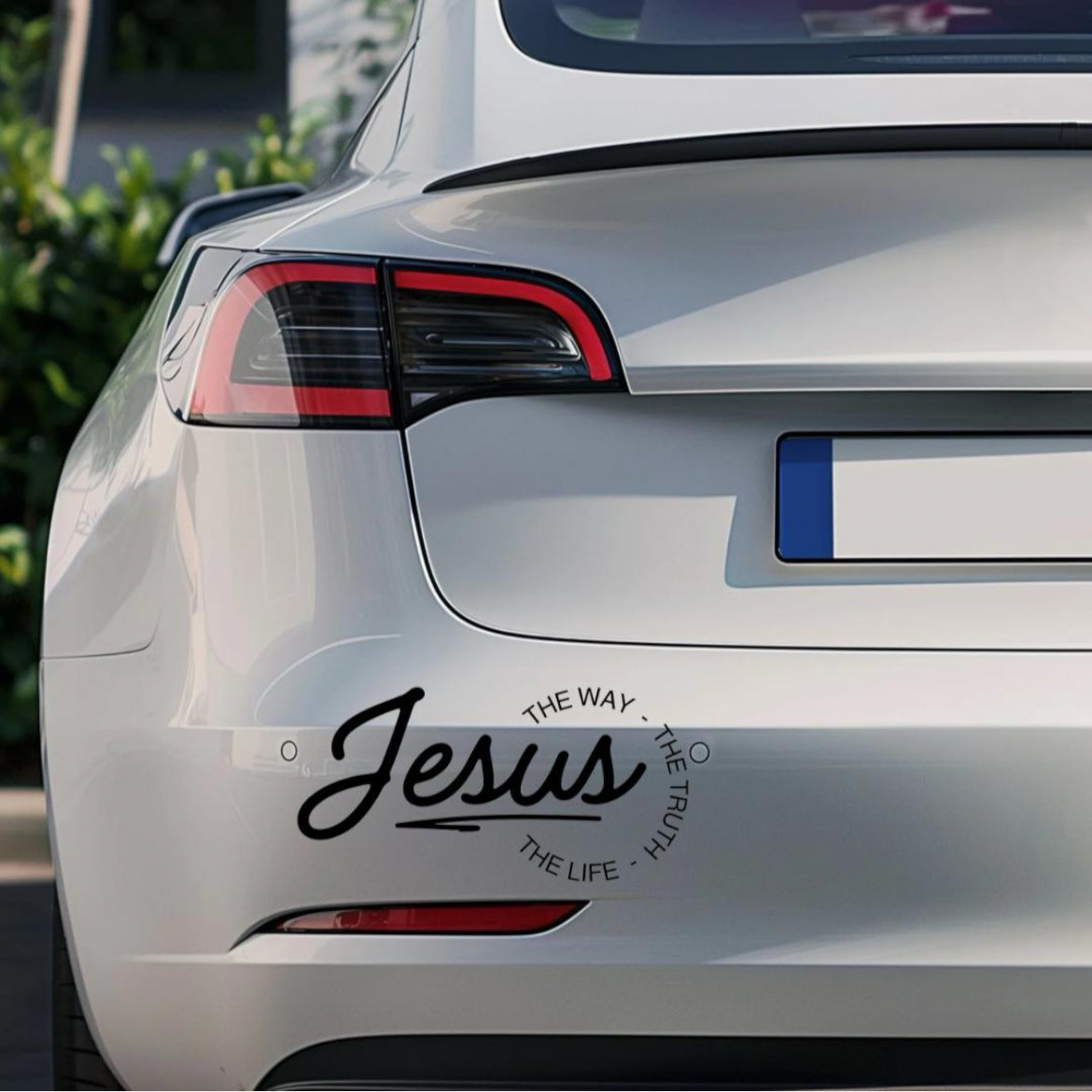 Bumper sticker car decal that says, “Jesus - the way, the truth, the life.” The word “Jesus” is in large cursive letters. The other words are in print and round the ending of “Jesus”.