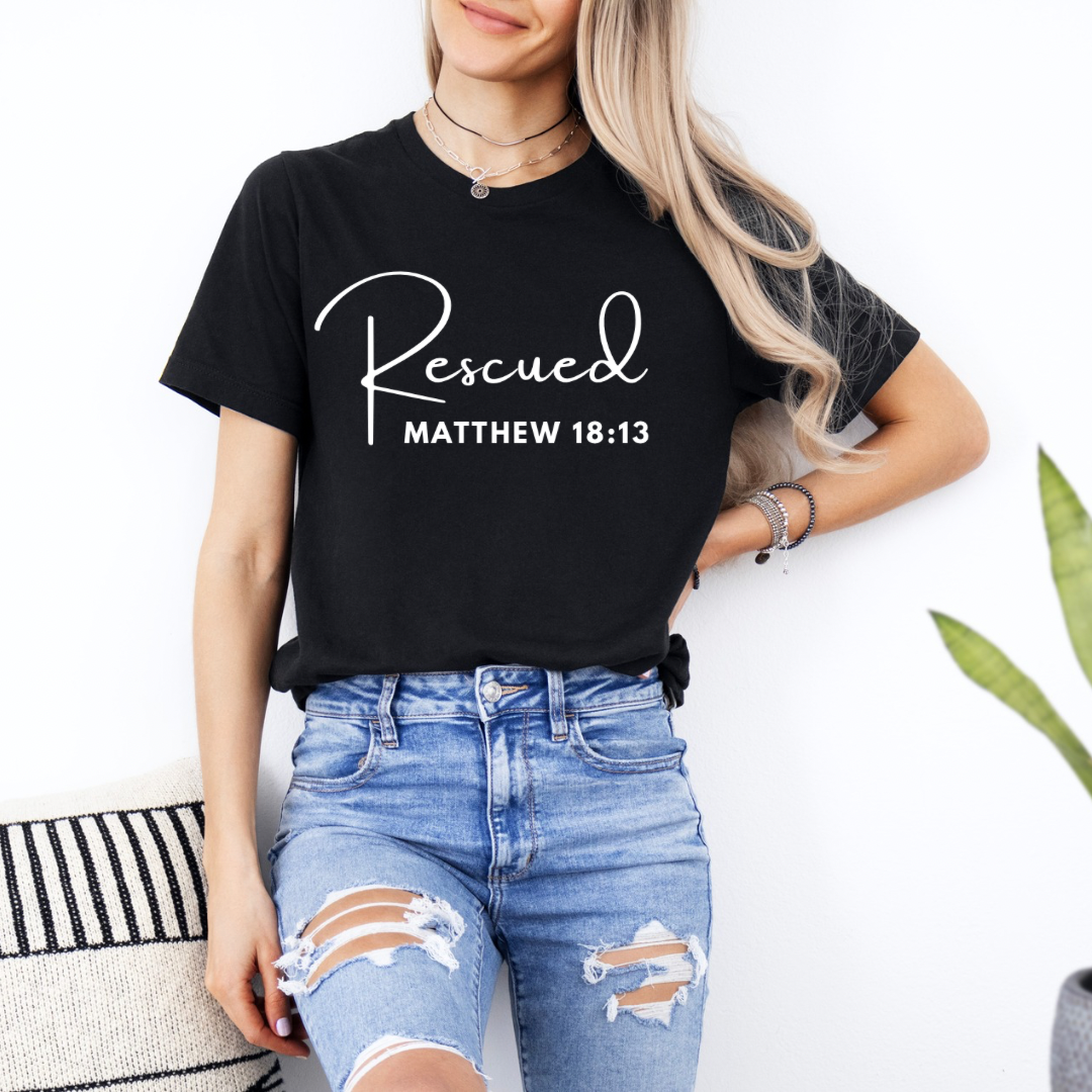 crewneck T-Shirt that says, "He left the 99 to rescue me". On the front it says, "Matthew 18:13 rescued" with a tan sheep.