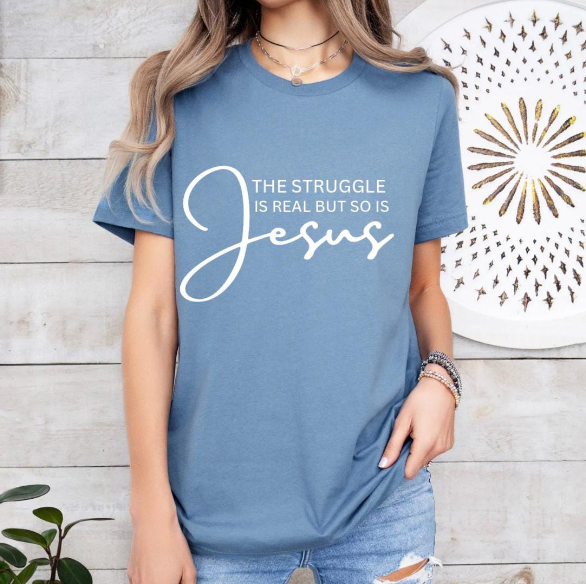 Steel blue crewneck t-shirt that says, “the struggle is real but so is Jesus”.