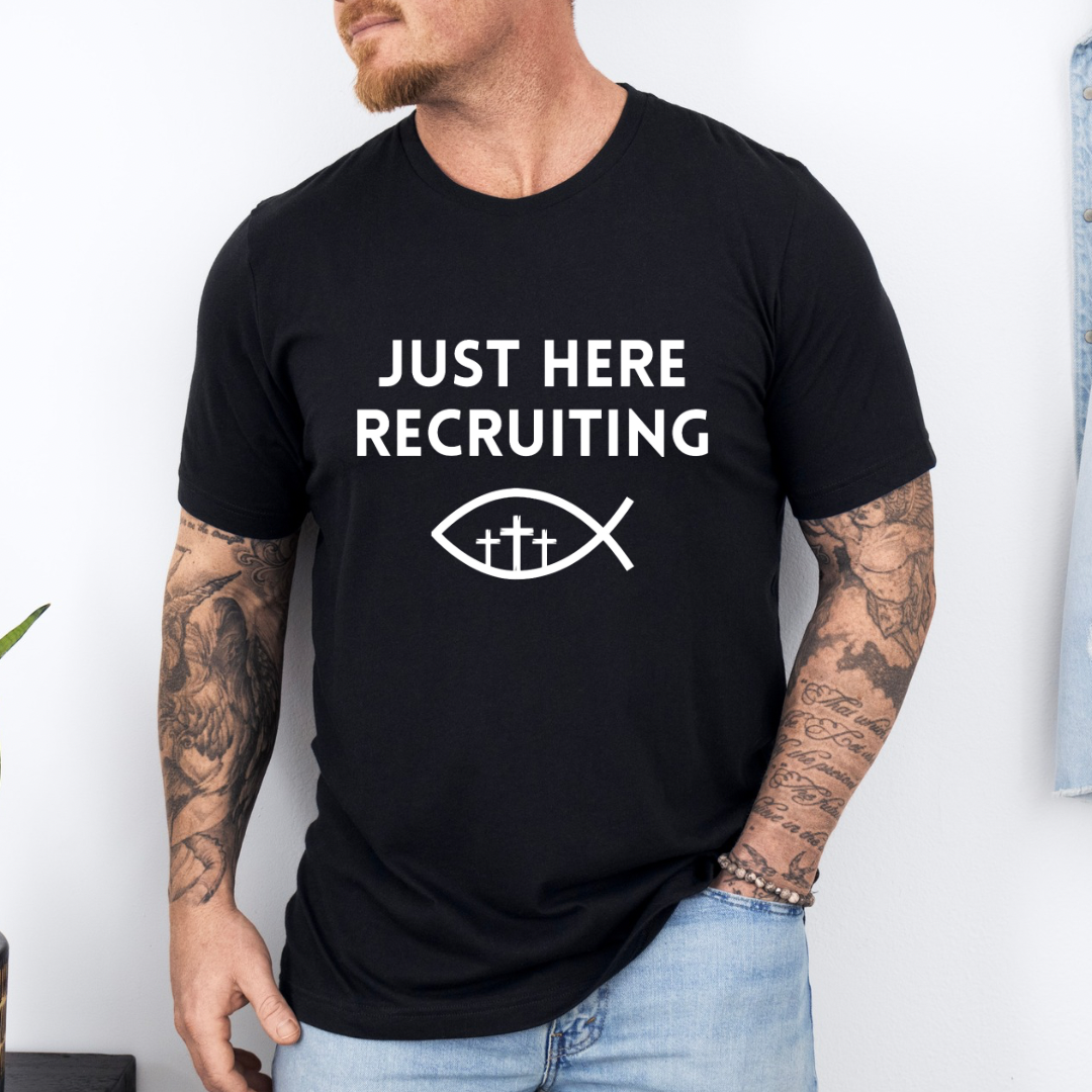 Black crewneck t-shirt that says, “just here recruiting” with the ichthus fish symbol. In the middle of the fish are three crosses.