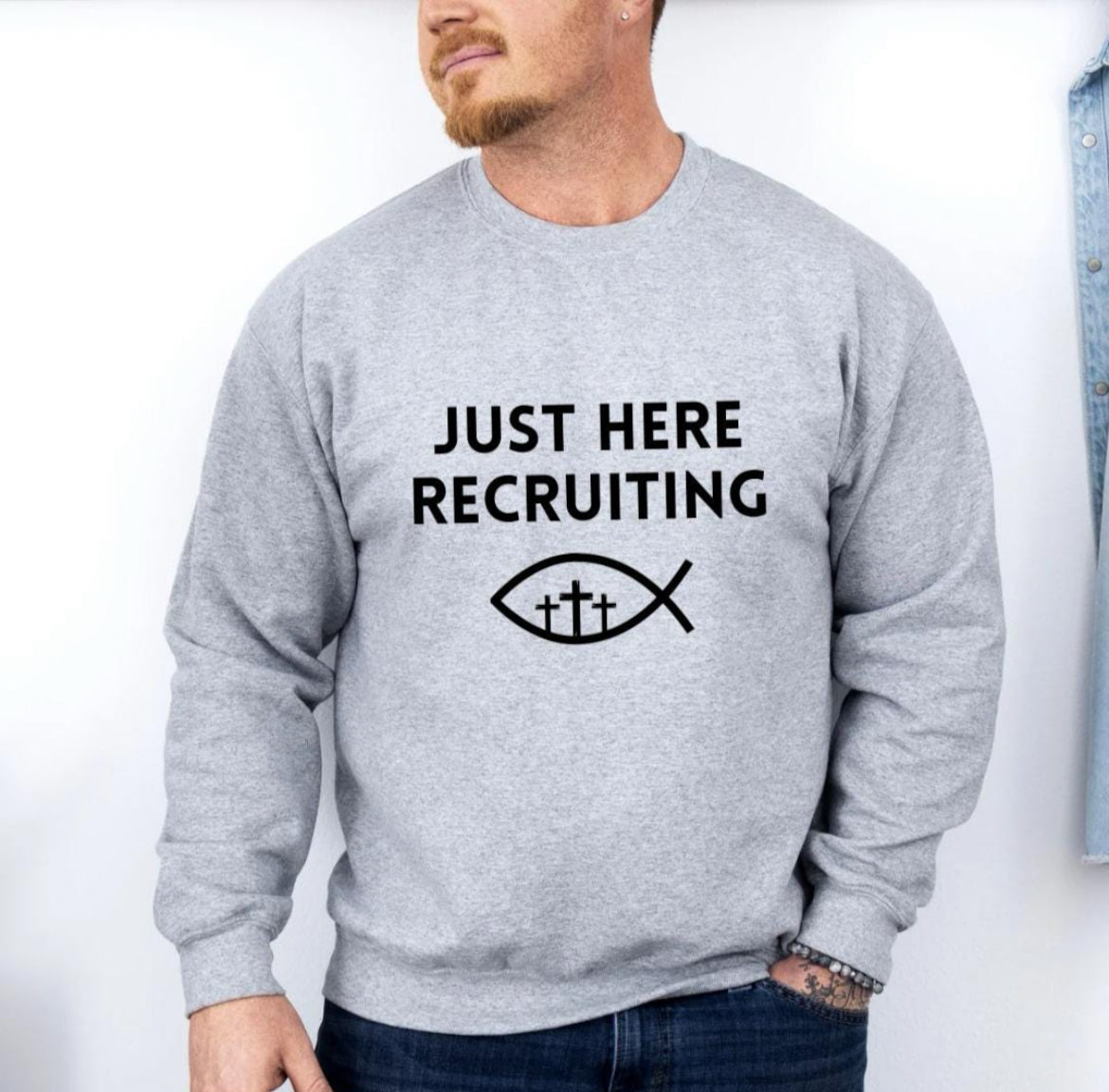 Light grey crewneck sweatshirt that says, "Just here recruiting" with the ichthus fish symbol with three crosses inside the fish.