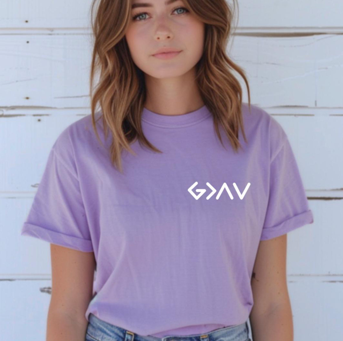 Lavender crewneck t-shirt with a cross on the back that has the symbol “God is greater than the highs and lows” as the bottom part of the cross.  The front has the same symbol in the upper left-hand corner.