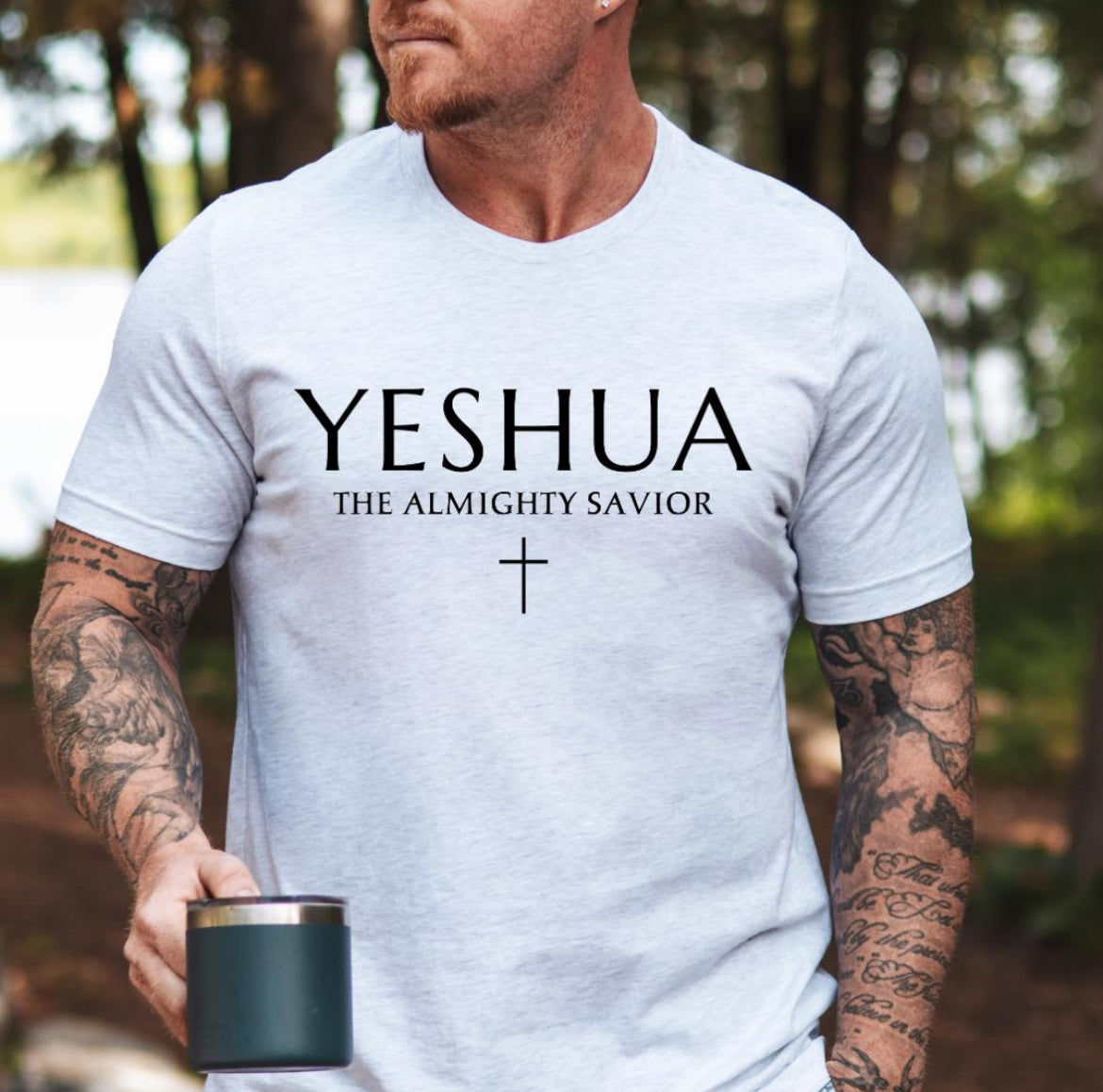 Ash white Crewneck T-shirt that says, “Yeshua” in large letters. Underneath in smaller letters it says, “the almighty savior” and under that is a small cross. 