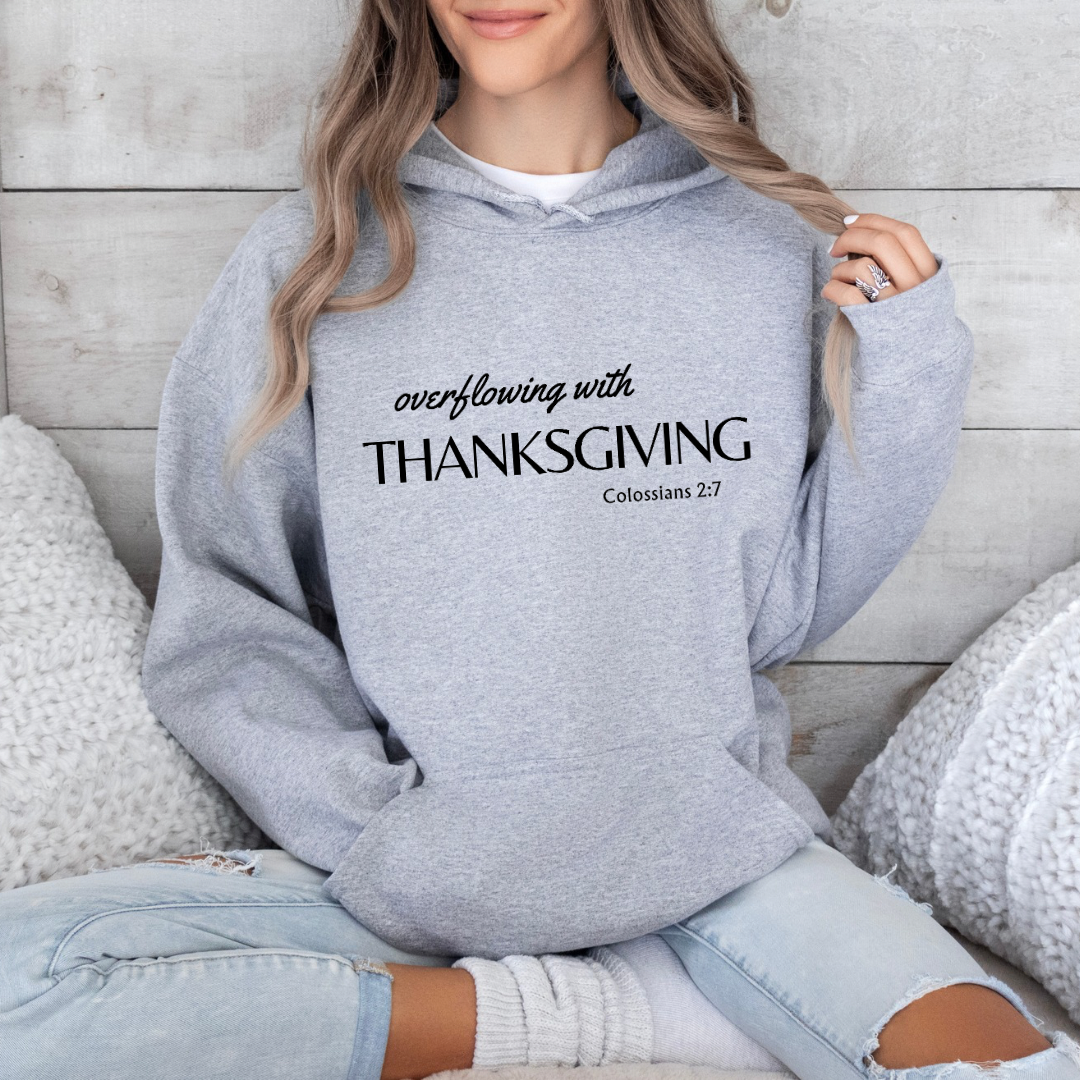 Gray hoodie sweatshirt that says, “overflowing with Thanksgiving. Colossians 2:7.”