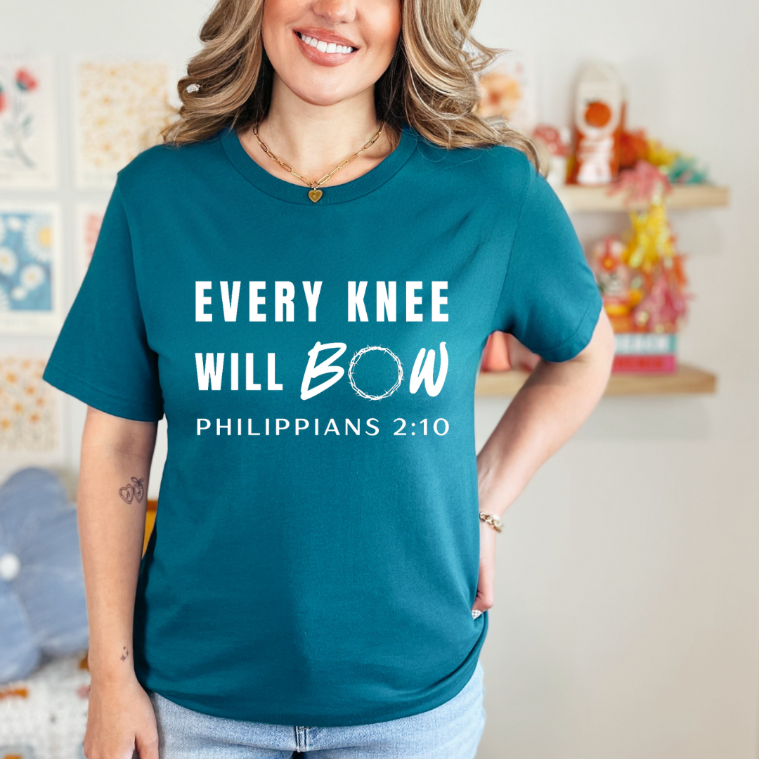 Deep teal crewneck t-shirt that says, “every knee will bow. Philippians 2:10” with a crown of thorns as the “o” in bow.