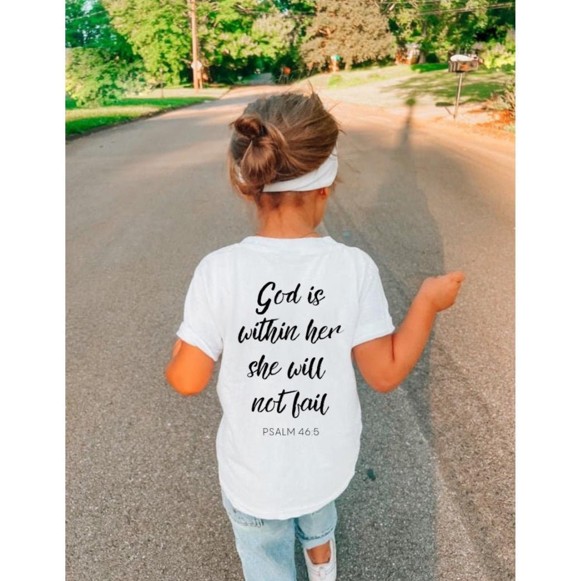 White Crewneck t-shirt that has a peace sign hand symbol made of bones in the upper left hand corner. On the back it says, “God is within her she will not fail.” Underneath in smaller letters it says, “Psalm 46 5.”