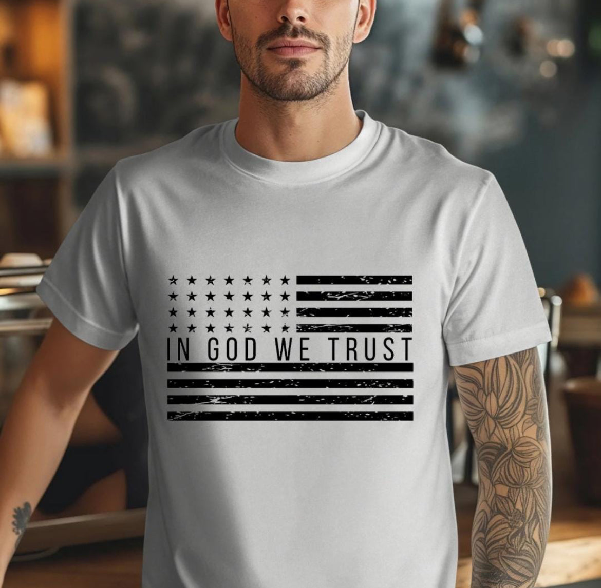 Grey crewneck t-shirt that has a distressed American flag. In the middle of the flag it says, “In God we trust.”