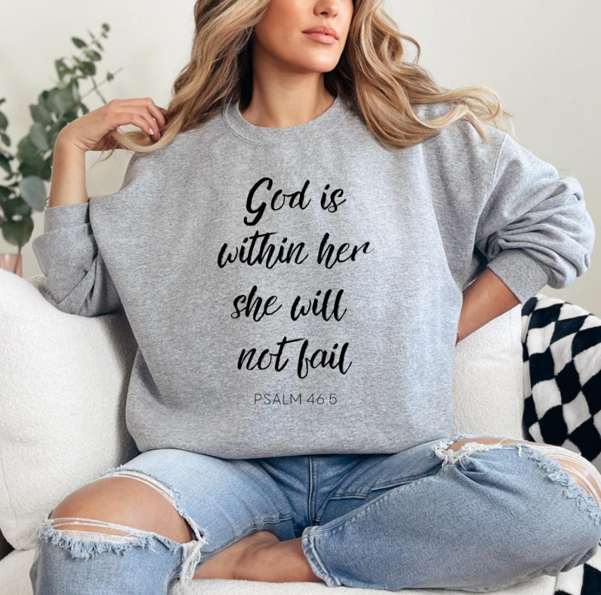 Light gray crewneck sweatshirt that says, "God is within her she will not fail." Underneath in smaller letters it says, "Psalm 46 5." On the sleeve there is a bones peace sing.