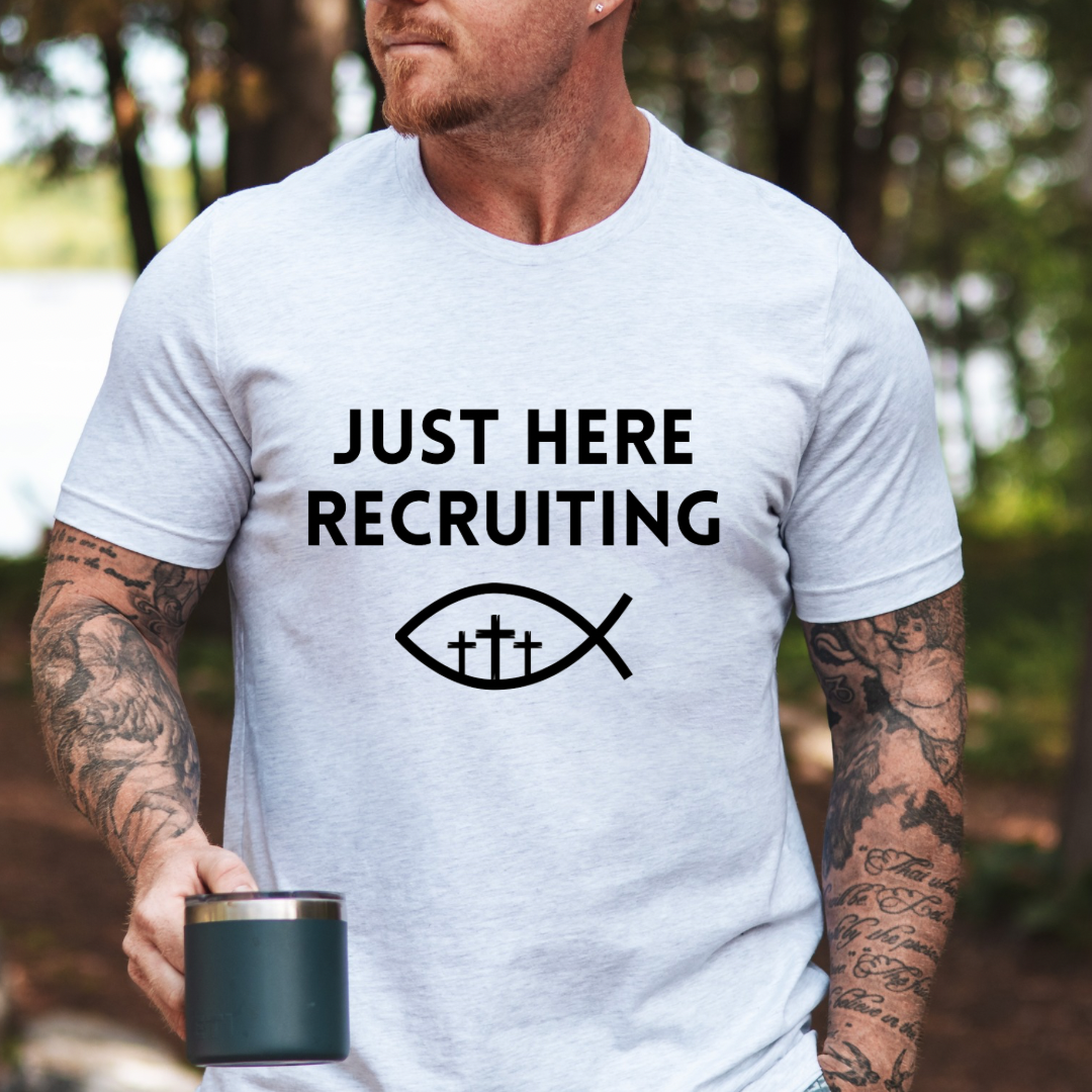 Ash white crewneck t-shirt that says, “just here recruiting” with the ichthus fish symbol. In the middle of the fish are three crosses.