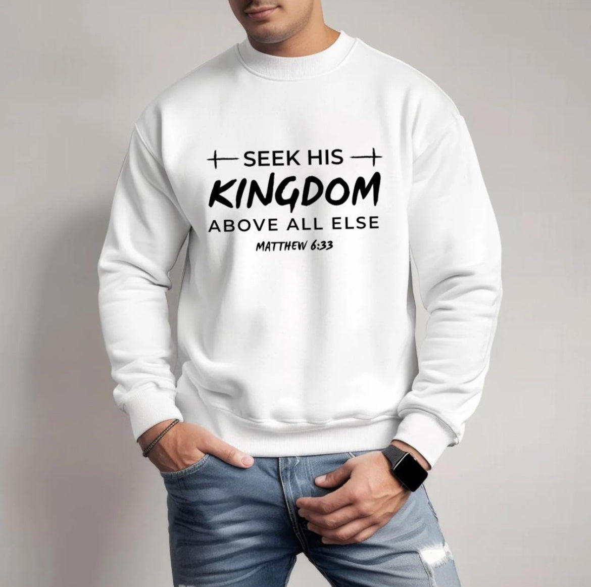 White crewneck sweatshirt that says, "Seek his Kingdom above all else." Underneath in smaller letters it says, "Matthew 6 33." There are two crosses as embellishments.