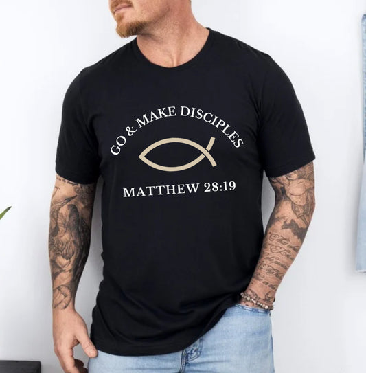 Black crewneck t shirt that says, "Go and make disciples, Matthew 28 19 on the front." On the back it says, "Let me tell you about Jesus." There is an ichthus Jesus fish symbol on the front and back. 