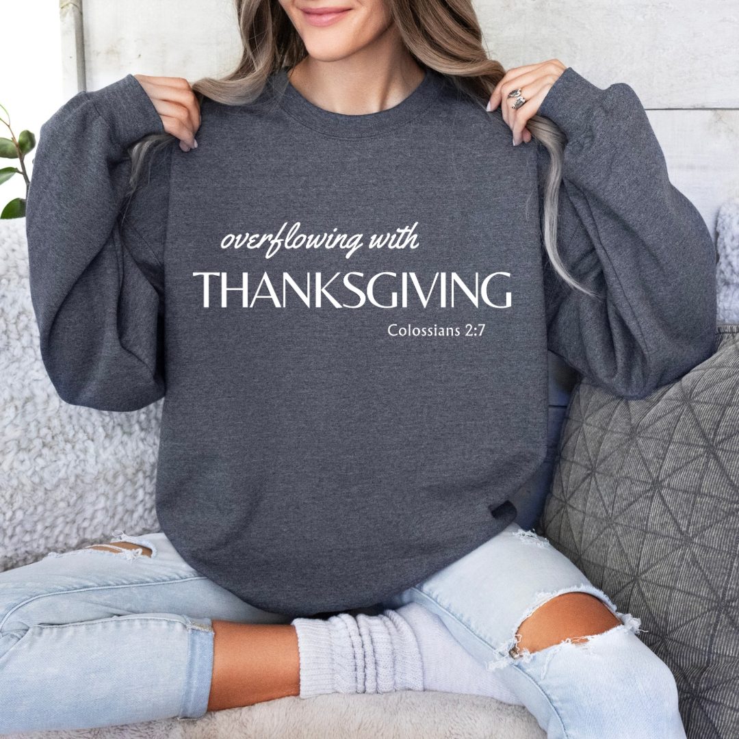 Heather gray crewneck sweatshirt that says, “overflowing with Thanksgiving. Colossians 2:7.”