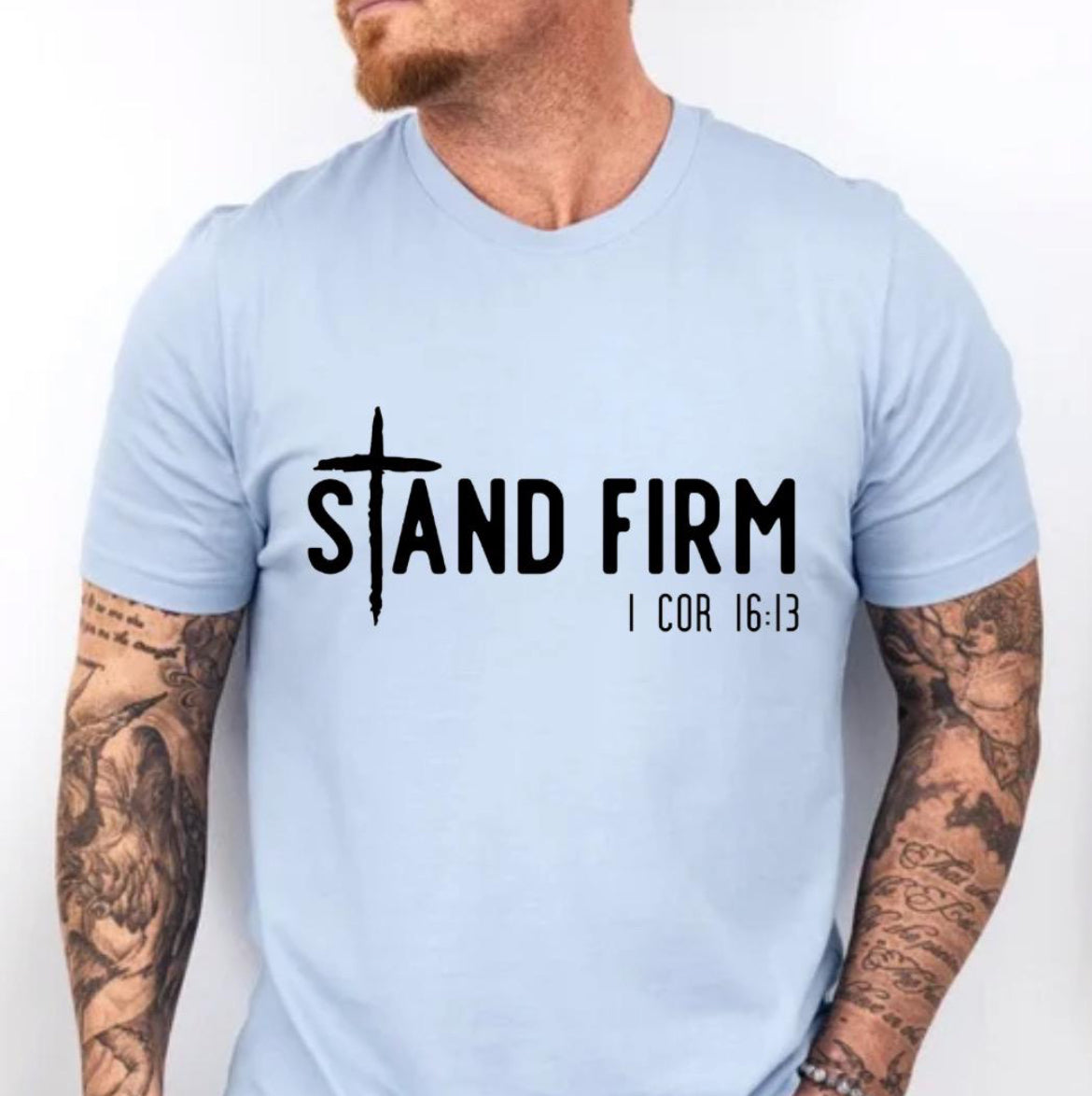 Baby blue Crewneck t-shirt that says, “Stand Firm” in large letters. The “t” in stand is a cross. Underneath in smaller letters it says, “1 Corinthians 16:13”.