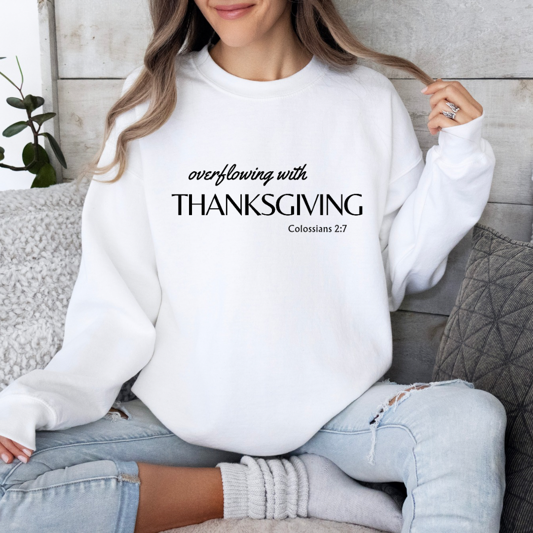 White Crewneck sweatshirt that says, “overflowing with Thanksgiving. Colossians 2:7.”