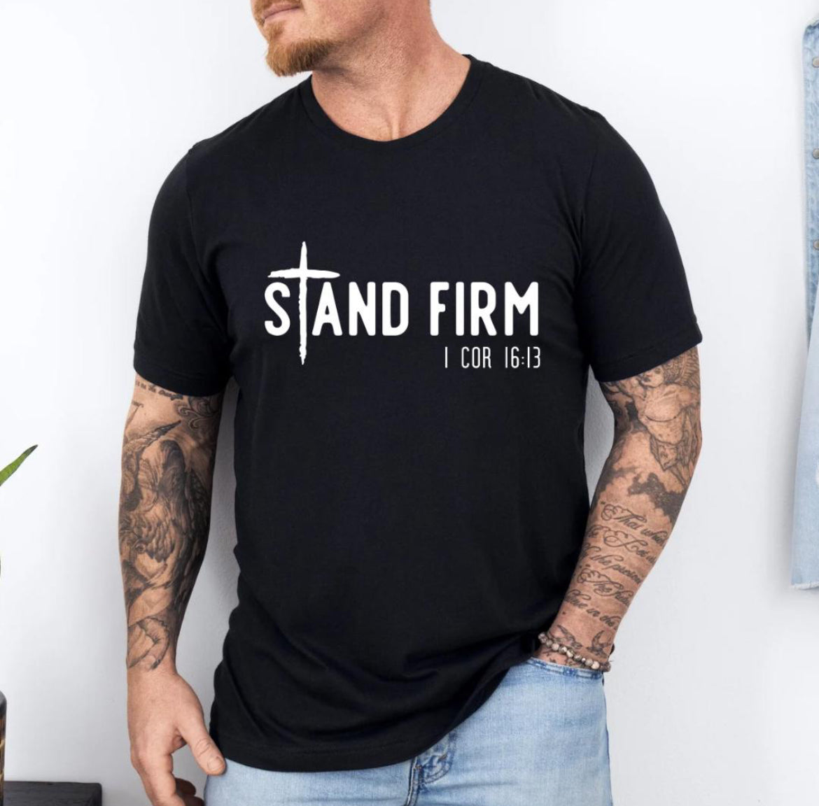 Black Crewneck t-shirt that says, “Stand Firm” in large letters. The “t” in stand is a cross. Underneath in smaller letters it says, “1 Corinthians 16:13”.