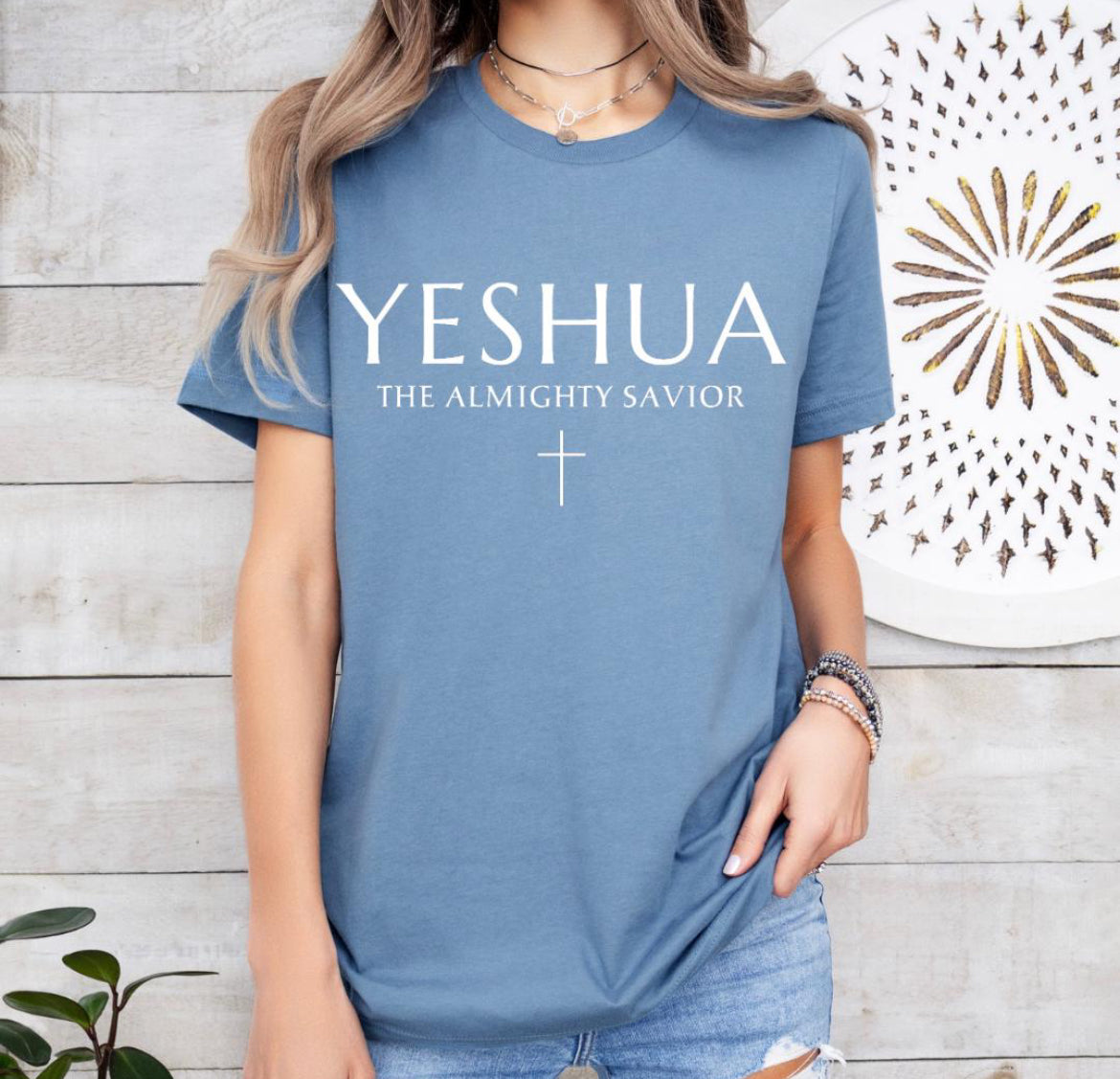 Steel blue Crewneck T-shirt that says, “Yeshua” in large letters. Underneath in smaller letters it says, “the almighty savior” and under that is a small cross. 