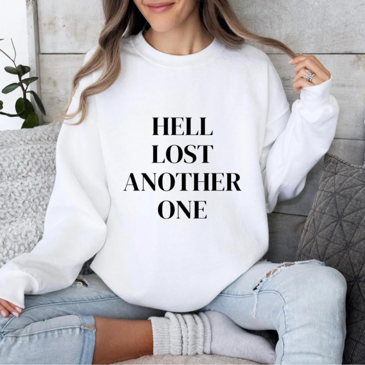 White crewneck sweatshirt that says, "Hell lost another one" on the front.