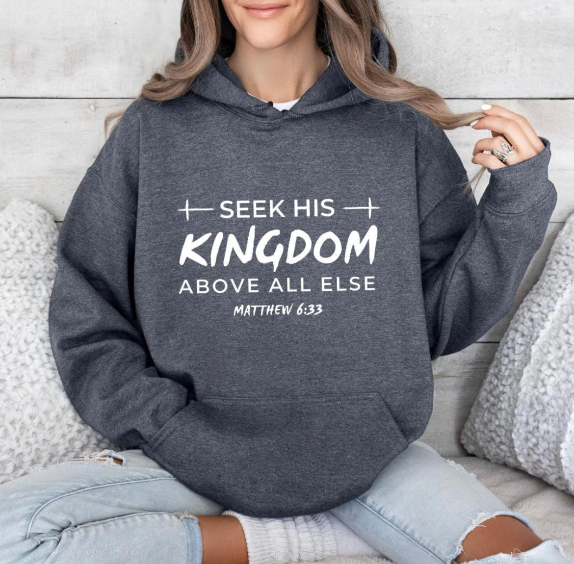 Dark gray hoodie that says, "Seek his Kingdom above all else." Underneath in smaller letters it says, "Matthew 6 33." There are two crosses as embellishments.