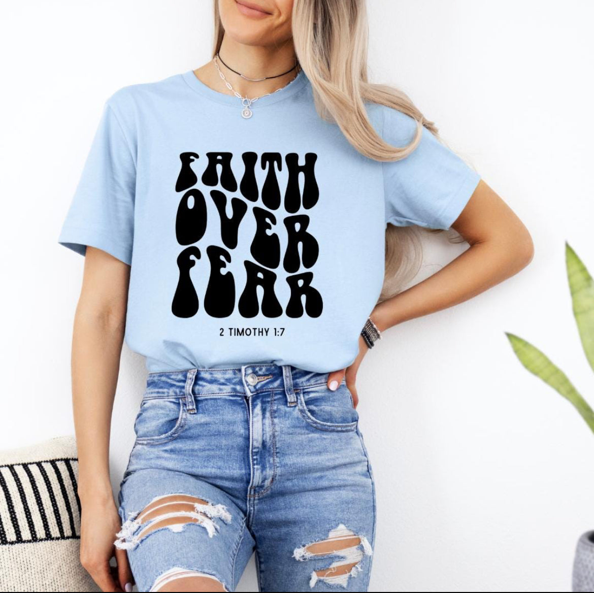 Baby blue crewneck t-shirt that says “faith over fear” in large bubble letters. Underneath in smaller letters it says, “2 Timothy 1 7.”