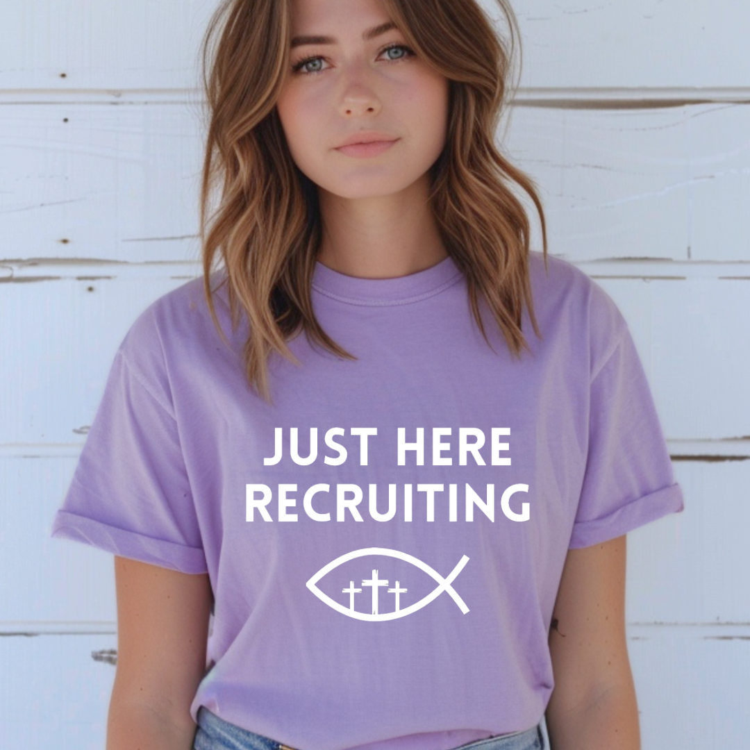 Lavender crewneck t-shirt that says, “just here recruiting” with the ichthus fish symbol. In the middle of the fish are three crosses.