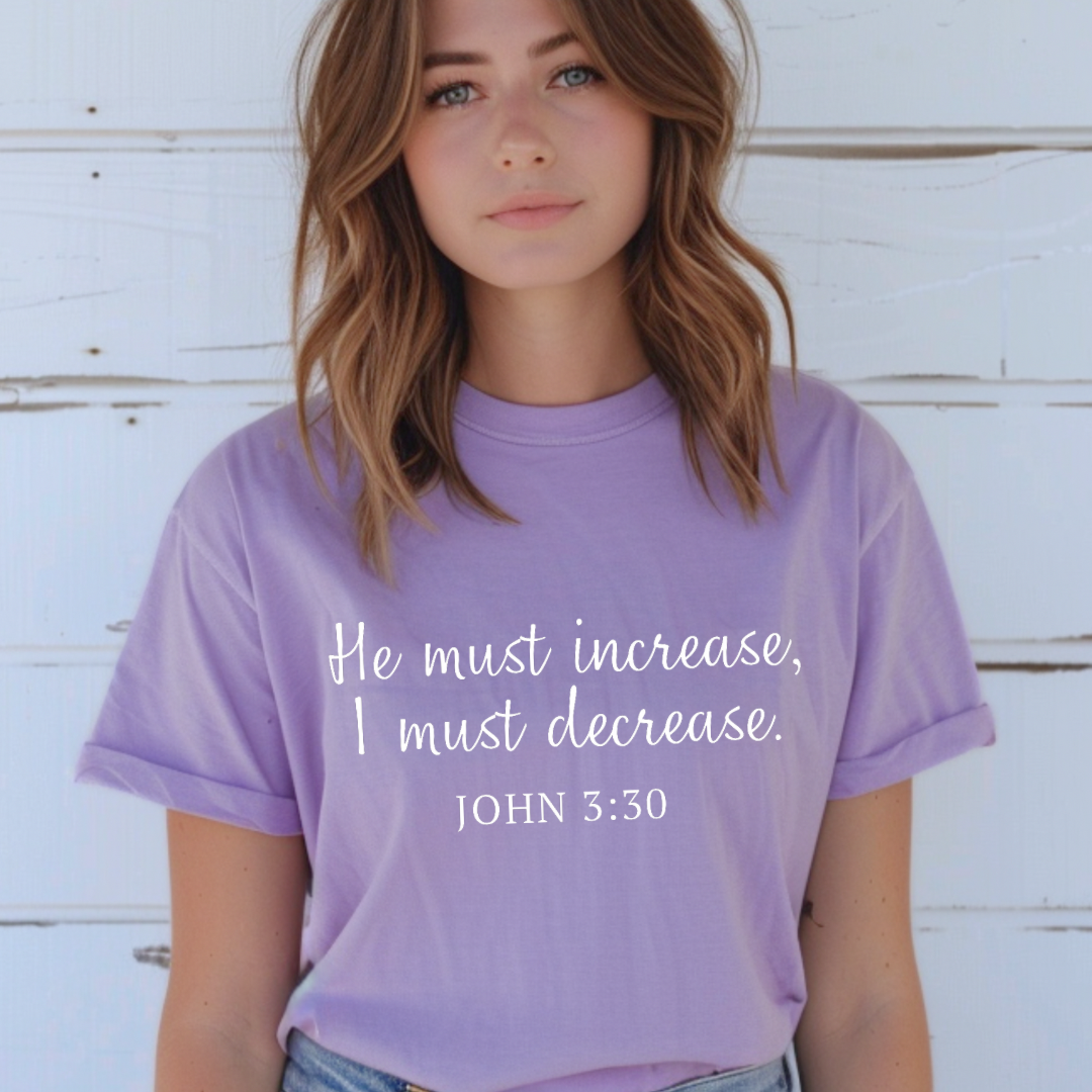 Lavender crewneck t-shirt that says, “He must increase, I must decrease.” Underneath in smaller letters it says, “John 3 30.”