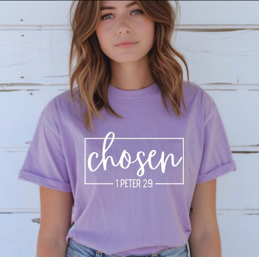 Lavender crewneck t-shirt that says, “chosen” in large cursive letters. Underneath in smaller letters it says, “1 Peter 2 9.”