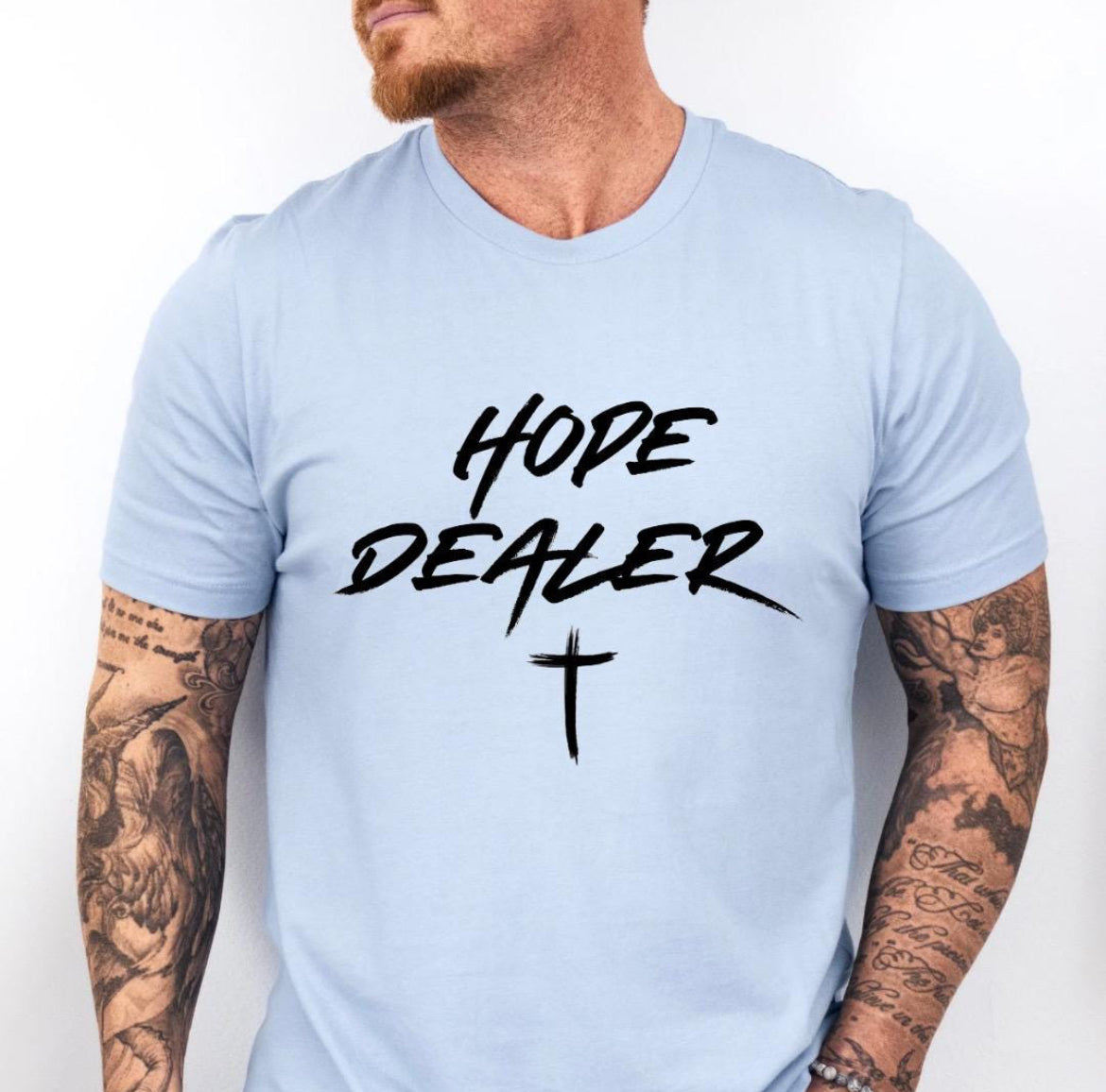 Baby blue crewneck t-shirt that says, “Hope dealer” in an urban graffiti style writing with a cross. 