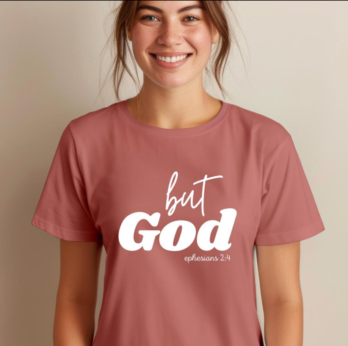 Mauve crewneck t-shirt that says, “but God” in large letters. Underneath in smaller letters it says, “Ephesians 2 4.”