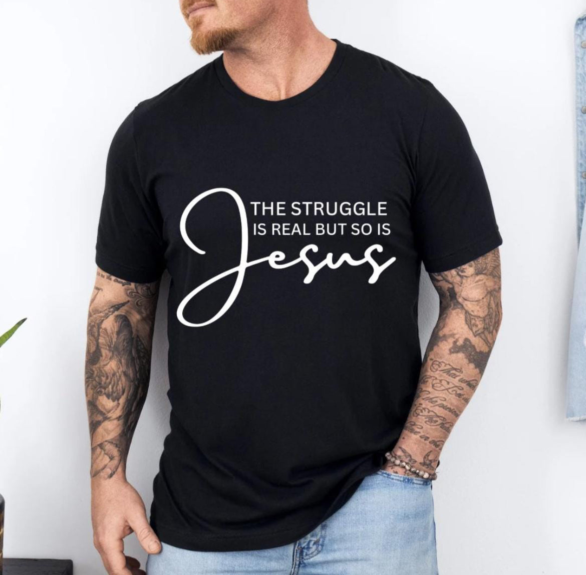 Black crewneck t-shirt that says, “the struggle is real but so is Jesus”.