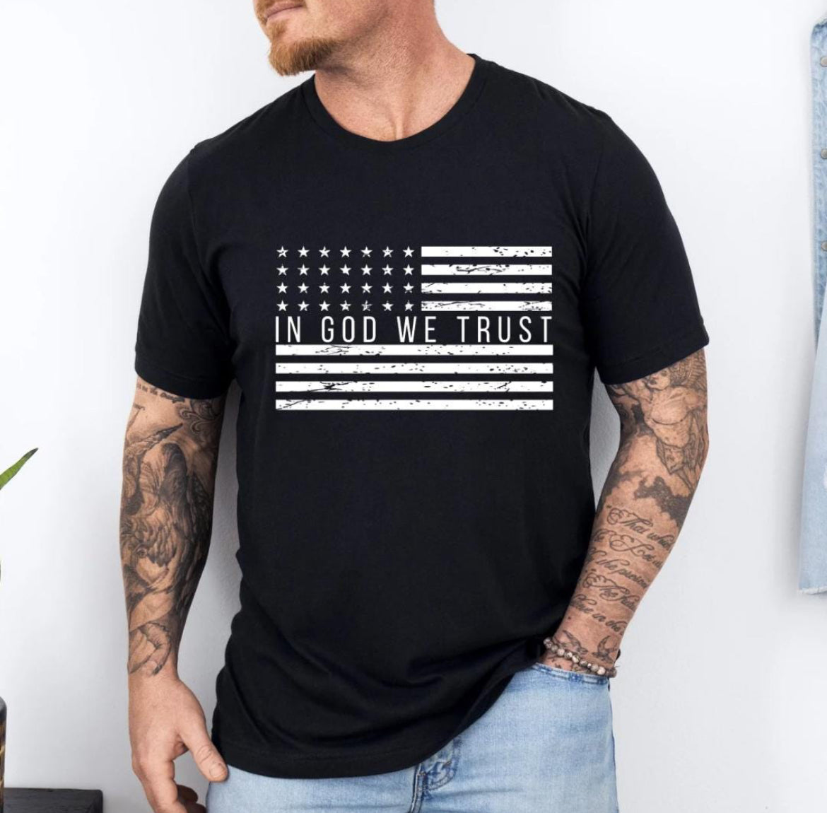 Black crewneck t-shirt that has a distressed American flag. In the middle of the flag it says, “In God we trust.”